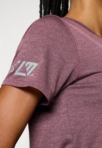 Top desportivo de mangas curtas, na cor ameixa, com um tecido texturizado, apresentando um design de logotipo e número na manga esquerda.