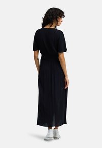 Μαύρο, μακρύ φόρεμα με κοντά μανίκια, εφαρμοστή μέση, ρέον φόρεμα και ελαφρύ ύφασμα. Συνδυασμένο με λευκά αθλητικά παπούτσια.