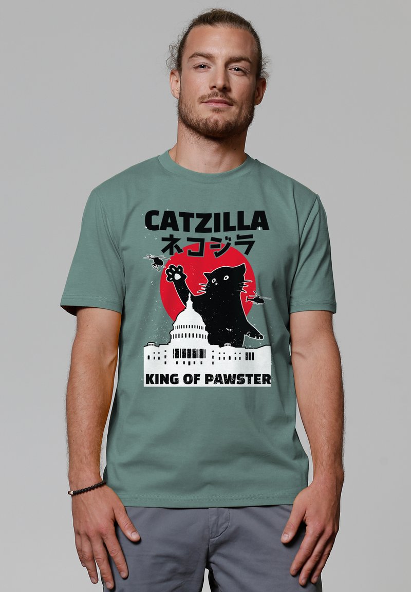 T-shirt vert à manches courtes avec un graphique d'un chat noir contre un cercle rouge, avec le texte "CATZILLA" et "KING OF PAWSTER" au-dessus et en dessous.