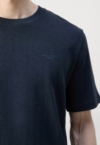 Tyrkysové tričko s krátkým rukávem vyrobené z bavlny, s kulatým výstřihem a nenápadným logem Marc O’Polo na levé hrudi. Hladká textura.