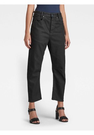 Vrouw die een zwarte rechte jeans met hoge taille draagt, gecombineerd met een donkerblauw mouwloos topje en zwarte sandalen met hak.