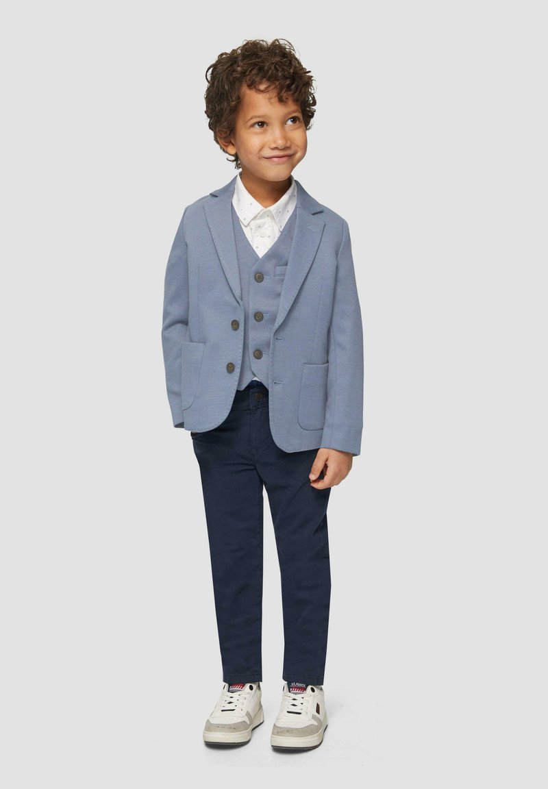 Hellblaues Blazer mit passender Weste, weißes Hemd mit Knöpfen, dunkelblaue Hose und weiße Sneakers mit grauen Akzenten. Glatte Stofftextur.