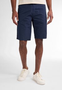 Shorts en coton bleu marine avec une coupe classique, dotés de poches latérales et d'un ourlet propre. Associés à des baskets blanches sur un fond uni.