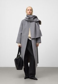 Grå ullkappa med en stor scarf-krage, med dubbelknappsstängning. Kombinerad med beige och svarta accessoarer. Slät textur, lös passform.