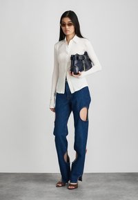 Λευκό πουκάμισο με μακριά μανίκια, σκούρο μπλε τζιν παντελόνι με φθορές και κοψίματα, και μοντέρνα τσάντα σε ναυτικό χρώμα με λουρί που κλείνει με αγκράφα. Καφέ ψηλοτάκουνα παπούτσια.