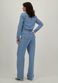 Lichtblauwe spijkeroutfit met een knoopsluiting top en wijde broekspijpen. De stof heeft een zachte textuur met een klassiek vijf-pocket ontwerp.