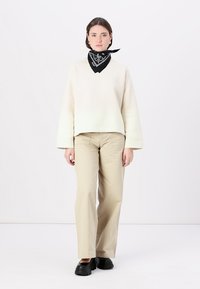 Felpa beige con texture e maniche ampie, abbinata a pantaloni beige. Una bandana nera è legata attorno al collo. Scarpe con plateau nere.