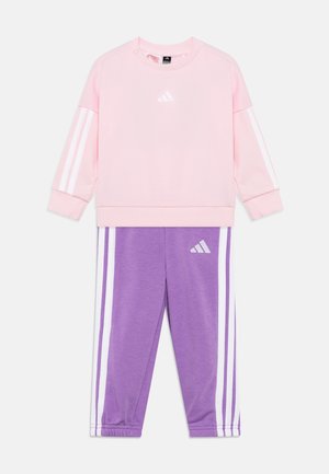 Felpa rosa con strisce bianche sulle maniche e logo; abbinata a pantaloni viola con strisce laterali bianche e logo. Tessuto morbido, design sportivo.