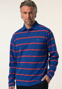 Långärmad polo i blått med kraftiga röda horisontella ränder. Har en knappad krage och en liten logotyp på bröstet. Mjuk textur.