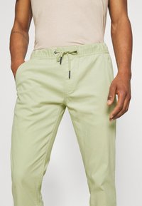 Light green elastic waist pants with a drawstring, featuring side pockets and a smooth cotton texture. Simple design with no patterns.