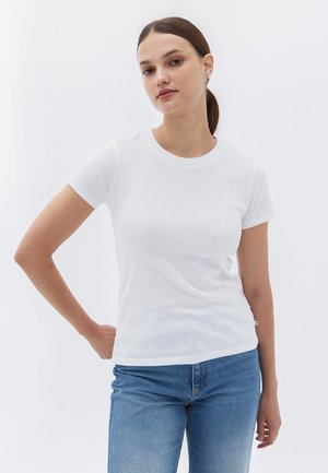 T-shirt en coton blanc avec col rond et manches courtes, assortie à un jean en denim bleu clair, présentée sur un fond blanc uni.