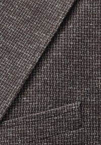 Texturiertes braunes Gewebe mit einem gewebten Muster in helleren Farbtönen. Enthält ein kleines Taschendetail. Weiche, strukturierte Oberfläche.