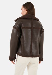 Hnedá umelá kožená bunda s fleece akcentmi, s širokým golierom, dlhými rukávmi a textúrovaným povrchom. Umiestnená s voľným strihom.