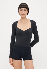 Body noir à manches longues avec un décolleté carré et un corsage ajusté doté de bonnets souples. Matière douce et extensible avec une texture lisse.