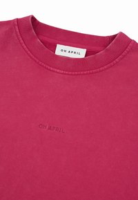 Lyserød crewneck sweatshir med ribbet krave, med diskret broderet tekst "OH APRIL" på brystet og en hvid mærkeetiket inde i nakken.