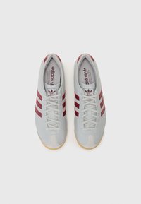Adidas sneakers med en lysegrå læderoverdel, tre burgunderstriber, flade snørebånd og en gummigummisål, der har et klassisk design.