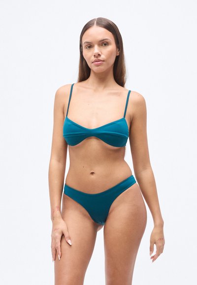 Σετ μαγιό μπικίνι σε τιρκουάζ χρώμα με τοπ bralette με λεπτές τιράντες και μπούτι μέτριας κάλυψης, και τα δύο κατασκευασμένα από απαλό ύφασμα. Απλός σχεδιασμός.