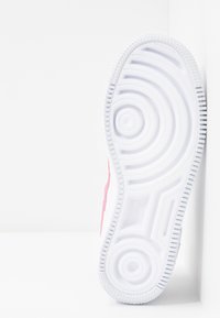 Semelle de chaussure blanche avec motifs de crampons circulaires et linéaires, positionnée verticalement sur un fond blanc.