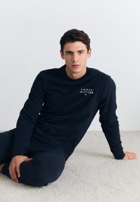 Námořnická košile s dlouhým rukávem a odpovídající kalhoty vyrobené z měkké tkaniny, s malým bílým logem "Tommy Hilfiger" na hrudi.