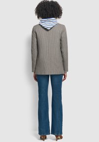 Marynarka w deseń houndstooth, z dopinaną, paskowaną kapturem, zestawiona z dzwonami niebieskimi dżinsami. Marynarka posiada wyraźnie zarysu sylwetkę i fakturowany materiał.