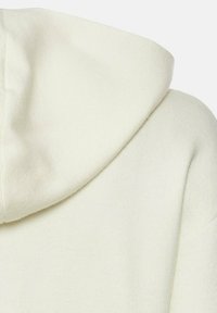 Crèmekleurige hoodie van een zachte, textuurstof. Heeft een ronde kap en zichtbare stiksels op de naden.