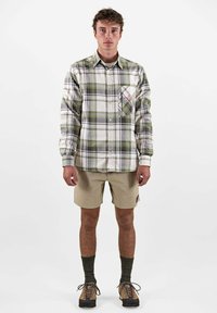 Karierte Button-Up-Hemd in Weiß, Grün und Grau, mit einer Brusttasche im Rautenmuster. Getragen mit beigen Shorts und braunen Schuhen.