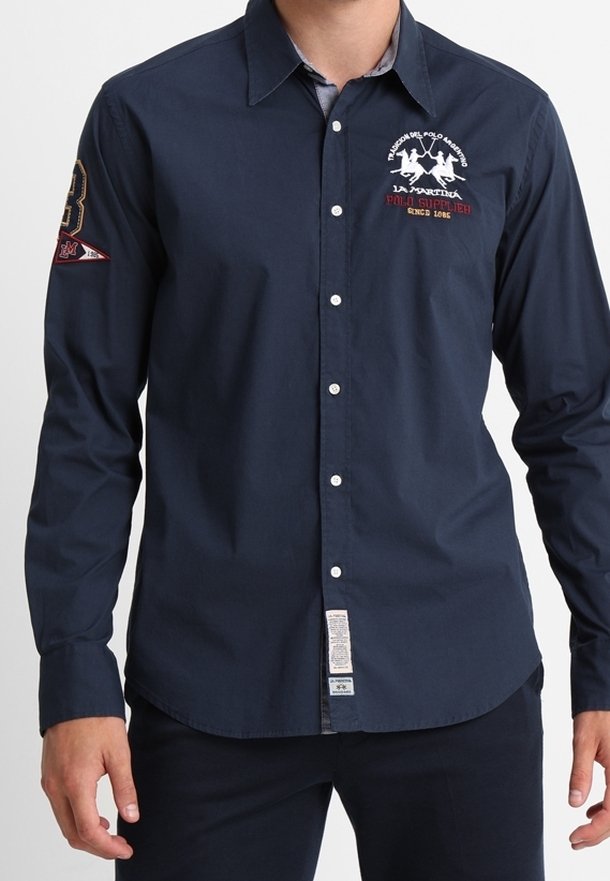 Camisa de manga larga azul marino con botones, fabricada en algodón. Cuenta con un logo en el pecho izquierdo y un parche con el número 3 en la manga derecha.