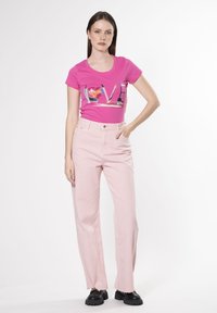 Camiseta fucsia con la palabra "AMOR" en lentejuelas, combinada con jeans de pierna ancha de color rosa claro y de cintura alta, y zapatos negros de suela gruesa.