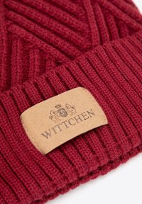 Berretto rosso lavorato a maglia con trama a coste e motivo diagonale. Presenta un'etichetta in pelle color cuoio con nome del marchio e logo in rilievo.