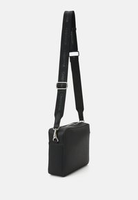 Borsa rettangolare nera con superficie testurizzata, zip argentata e tracolla regolabile con il logo "Valentino".