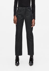 Zwarte en grijs gemarmerde high-waisted jeans met rechte pijpen, vijf zakken en zichtbare stiksels. Draagt het met glanzende zwarte enkellaarsjes.