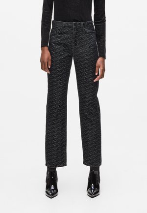 Black and gray patterned high-waisted jeans with straight legs, five pockets, and visible stitching details. Worn with glossy black ankle boots.