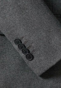 Tissu en laine gris à la texture lisse. Quatre boutons noirs sur le poignet d'une veste de costume, détaillés avec des points de chaînette.