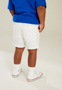 White cotton shorts, blue t-shirt, and white high-top sneakers. Visible pockets on shorts and textured fabric on the shirt.