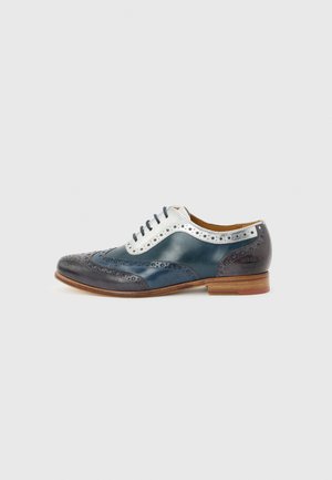 Chaussure brogue homme en cuir bleu marine, blanc et gris foncé avec perforations décoratives et semelle marron clair, vue de profil.