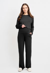 Schwarzes Langarmoberteil mit gekürztem Design, kombiniert mit schwarzen weit geschnittenen Hosen mit Seitentaschen und einer glatten Textur.