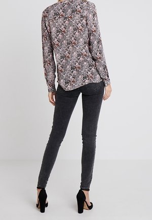 Langärmlige Bluse mit Blumenmuster in Pink, Schwarz und Weiß, kombiniert mit grauen Skinny-Jeans. Strukturierter Stoff, dezentes Muster, abgerundet mit schwarzen High Heels.