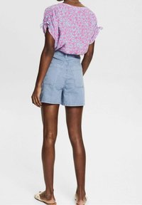 Lichtblauwe denim shorts met twee achterzakken, gecombineerd met een roze bloemen top met geplooide mouwen en strikjes op de schouders.