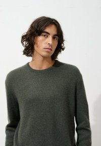 Dunkelgrüner Pullover aus weichem, strukturiertem Stoff. Mit Rundhalsausschnitt und langen Ärmeln, in einem schlichten, unauffälligen Design.