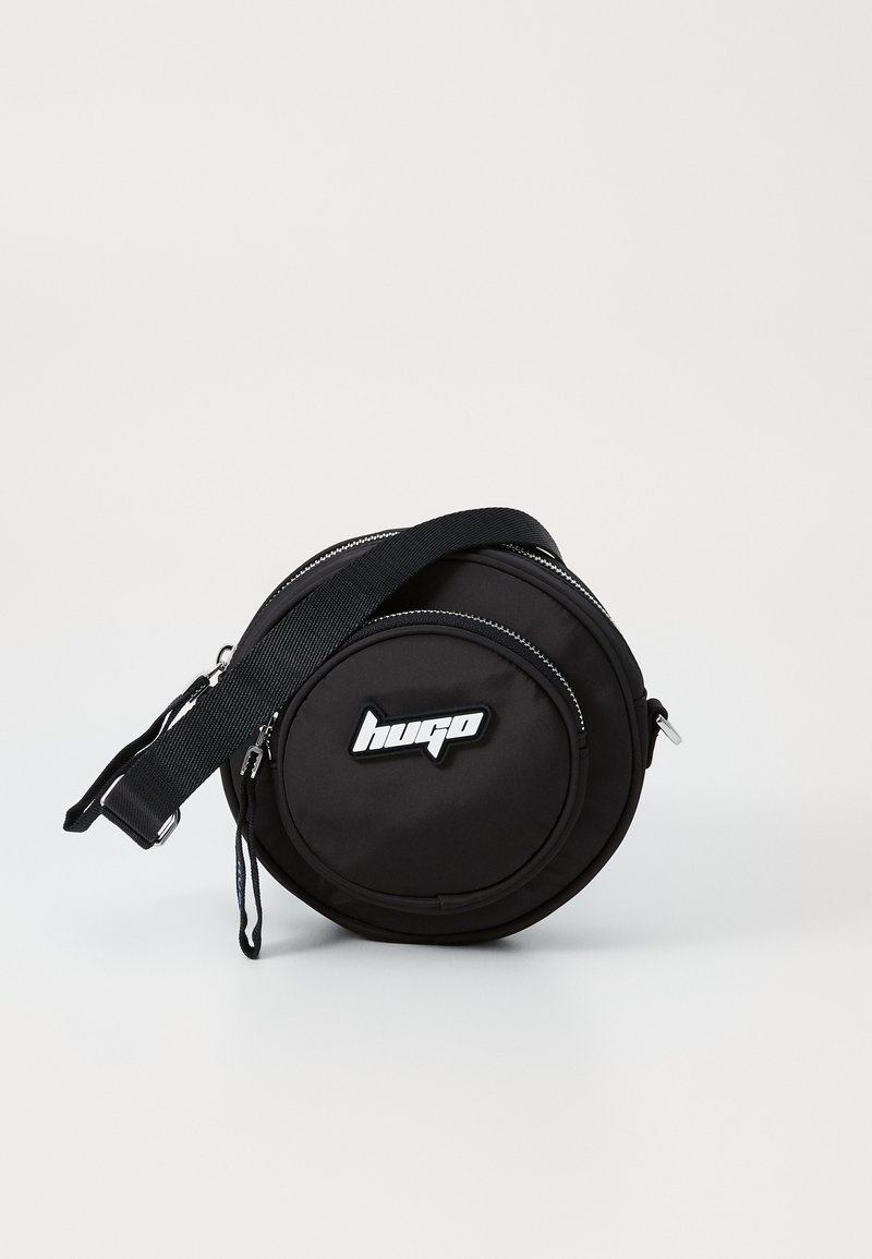Czarna okrągła torba na ramię wykonana z wytrzymałego materiału, z podwójnymi zamkami błyskawicznymi, wyściełanym regulowanym paskiem i naszywką z logotypem z przodu.