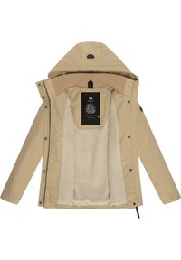 Beige ytterjacka med foder av päls. Har en stor huva, dragkedja och tryckknappar. Inuti finns en etikett som visar en logotyp och designinformation.