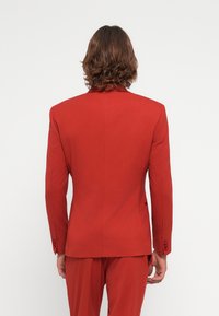 Rød dressjakke laget av glatt stoff, med en skreddersydd passform, hakkede lapels, to knapper og enkelt splitted bak.