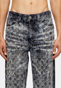 Jean en denim usé avec une palette de couleurs bleue et grise, surface texturée avec des détails effilochés et poches avant. Fermeture à bouton en métal.