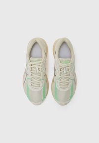 Beige Mesh-Sneaker mit hellgrünen und grauen Akzenten, mit einer strukturierten Oberseite, Schn�ürdesign und Gummisohle.
