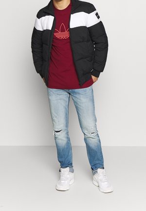 Doudoune noire et blanche, t-shirt rouge avec motif graphique, jean bleu clair déchiré et baskets blanches. Tenue décontractée, coupe moderne.