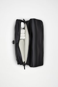 Μαύρη ορθογώνια τσάντα με φερμουάρ, με λεία υφή. Το εσωτερικό αποκαλύπτει ανοιχτό μπεζ φόδρα, ένα ασημένιο μπουκάλι και τυλιγμένες πετσέτες.