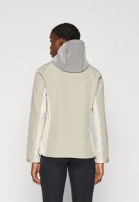 Veste gris clair avec capuche texturée et à motifs. Présente un design ajusté, des manches longues et des accents blancs sur les côtés pour plus de détails.