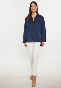 Camicia button-up blu navy con colletto, maniche lunghe e vestibilità comoda, abbinata a pantaloni color crema e mocassini marrone chiaro.