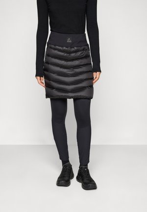 Svart puffer skjørt med chevronmønster, elastisk midjebånd, glidelåslommer, brukt over svarte leggins og svarte sko.