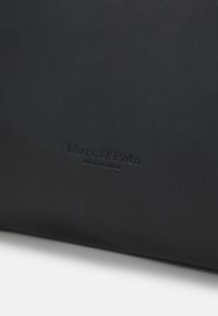 Czarna skórzana torba o gładkiej fakturze i dyskretnym logo, które brzmi "Marc O'Polo EST. W Sztokholmie" wytłoczone na powierzchni.